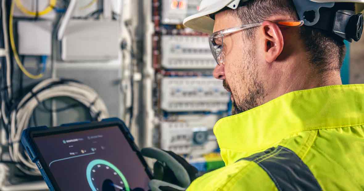 Un technicien travaille sur une alimentation stabilisée pour assurer la sûreté des équipements avec une tablette.